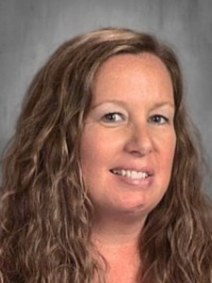 Portrait of a smiling woman with long wavy brown hair against a gray background.